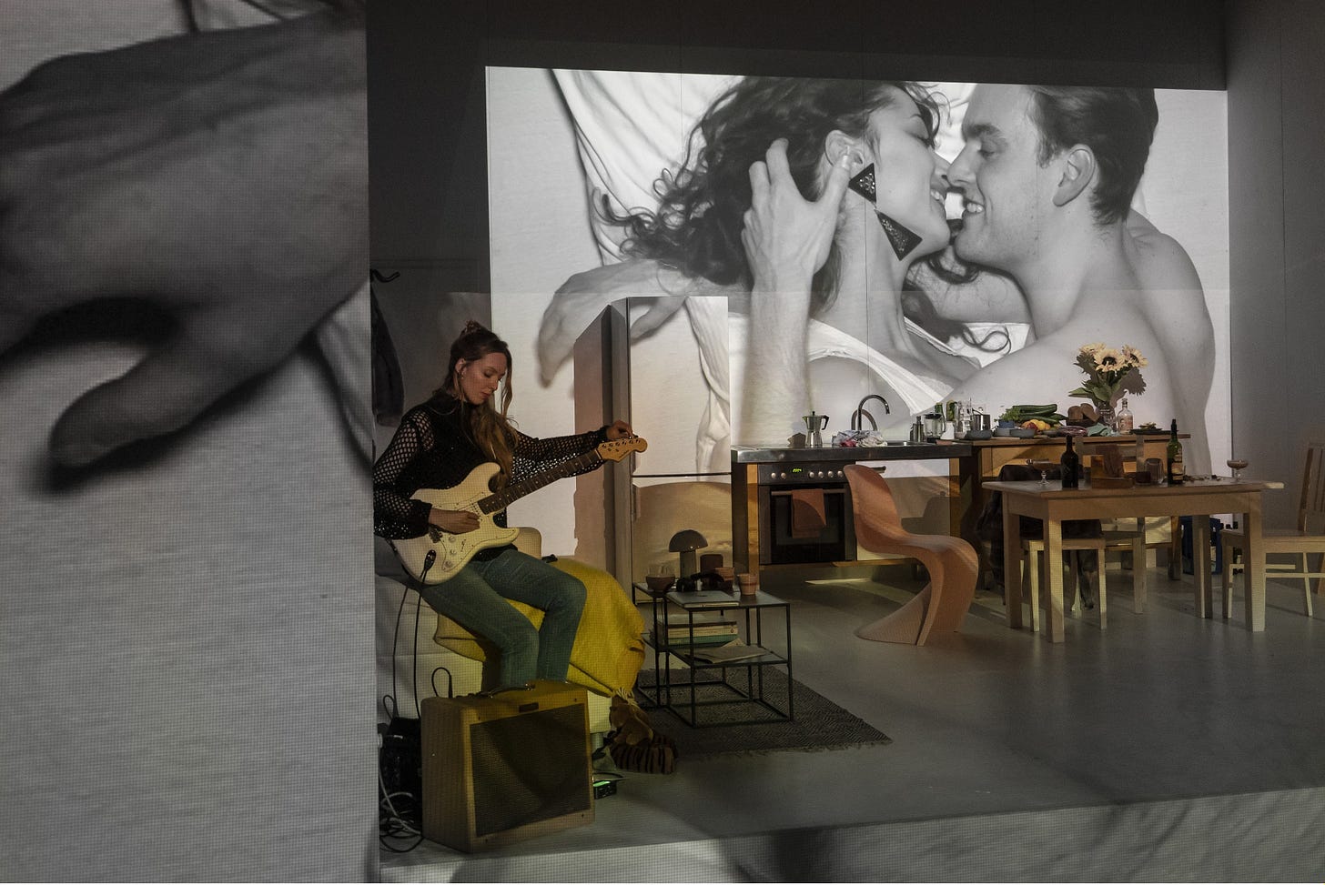 A woman plays a guitar in an apartment on the wall of which we can see  a projection of two lovers.