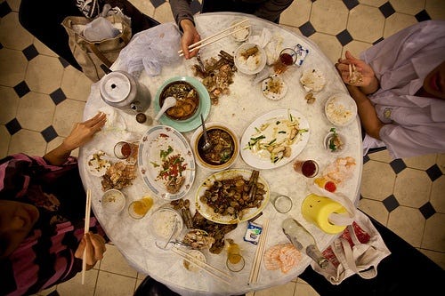 This may contain: several people sitting around a table with food on it