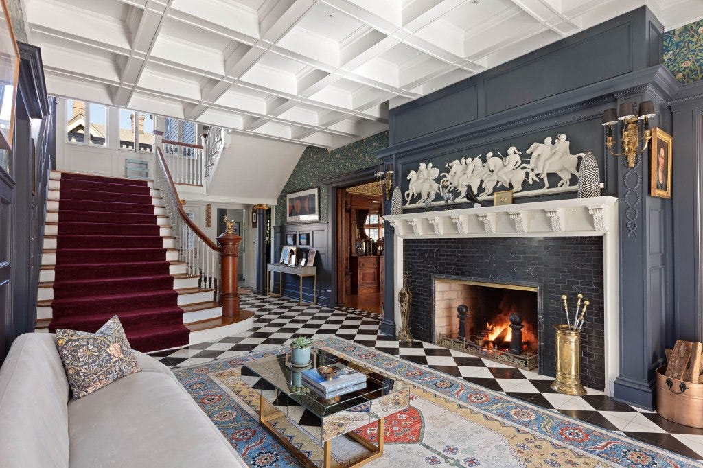 The entryway features a coffered ceiling, the grand staircase and one of several fireplaces in the home.