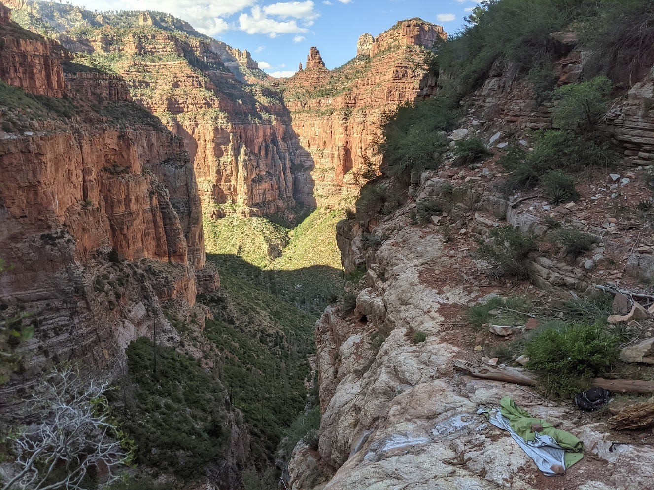 A sleeping bag and sleeping pad right at the edge of a cliff. Large impressive red cliffs in the distance.