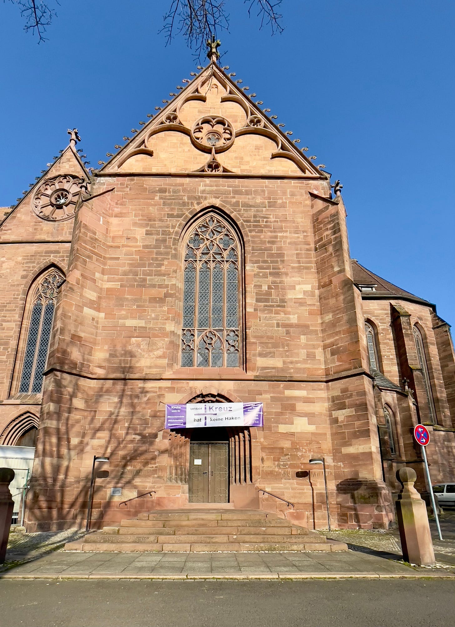Full view of the façade of the Münsterkirche St. Alexandri, a late Gothic hall church in Einbeck, Germany. A purple and white banner is hung above the main entrance, stating: “Unser Kreuz hat keine Haken” (“Our cross has no hooks”). The church features pointed arch windows, sandstone walls, and architectural details from its construction between 1275 and 1506. Full view of the façade of the Münsterkirche St. Alexandri, a late Gothic hall church in Einbeck, Germany. A purple and white banner is hung above the main entrance, stating: “Unser Kreuz hat keine Haken” (“Our cross has no hooks”). The church features pointed arch windows, sandstone walls, and architectural details from its construction between 1275 and 1506.