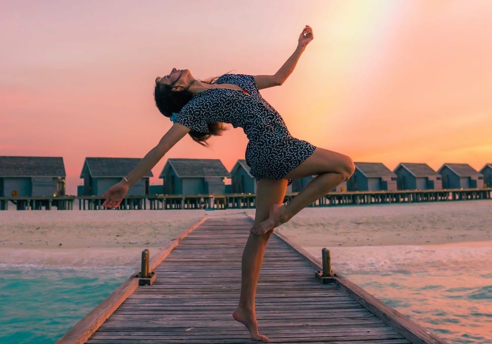 Vibrant healthy woman dancing on the end of a pier at sunset