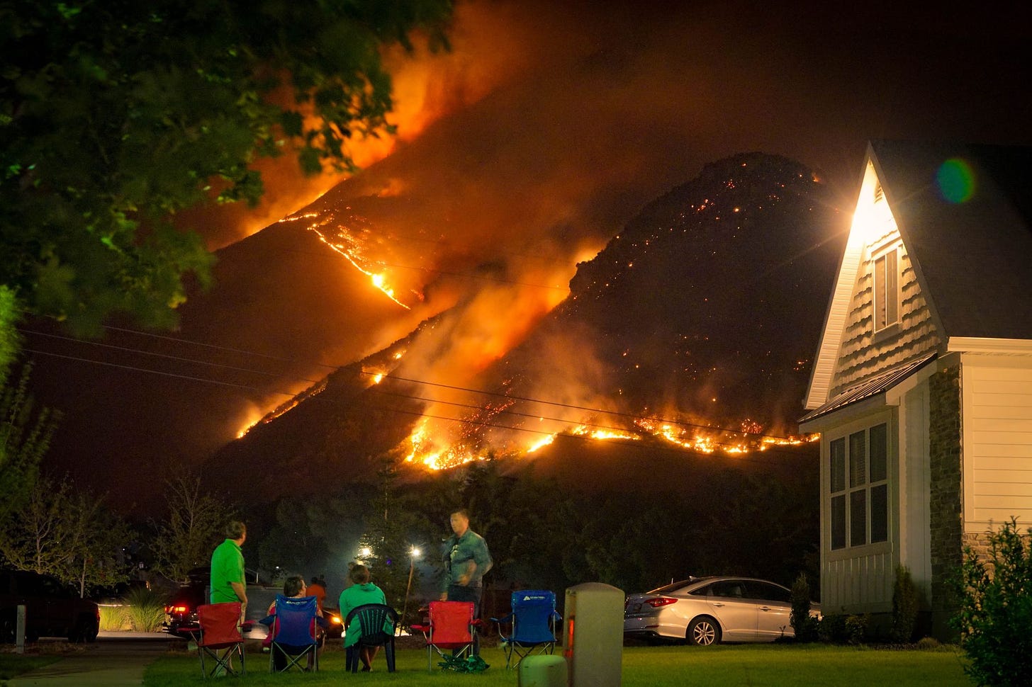 Family sitting outside casually watching a mountain on fire.