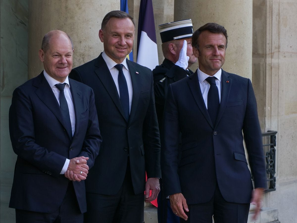 Three leaders standing in front of the palace as a soldier salutes behind them.