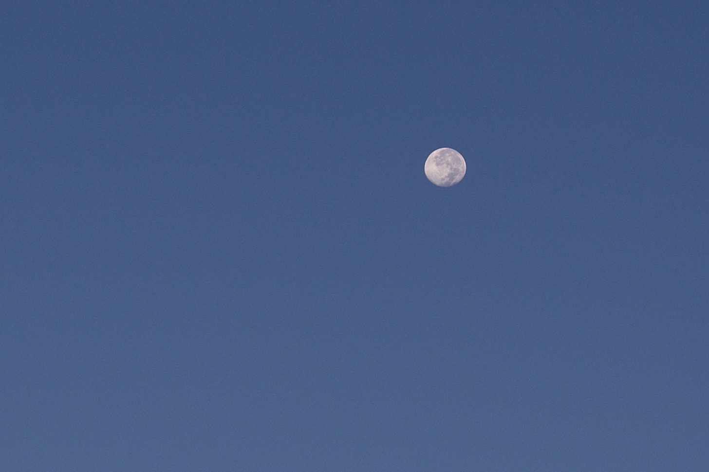 The full moon setting in the blue morning sky