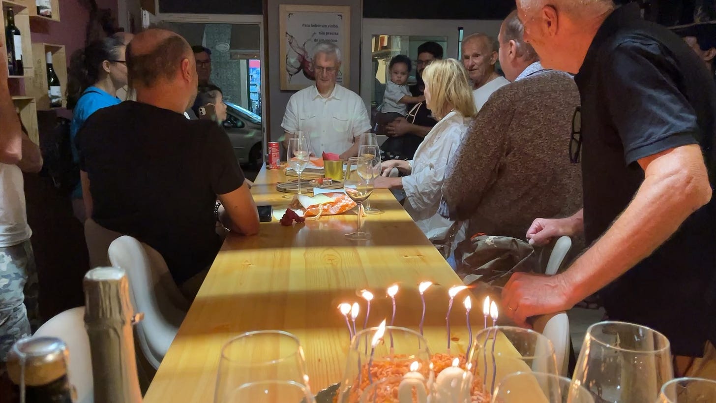80th Birthday Party cake with candles, glasses and people standing round