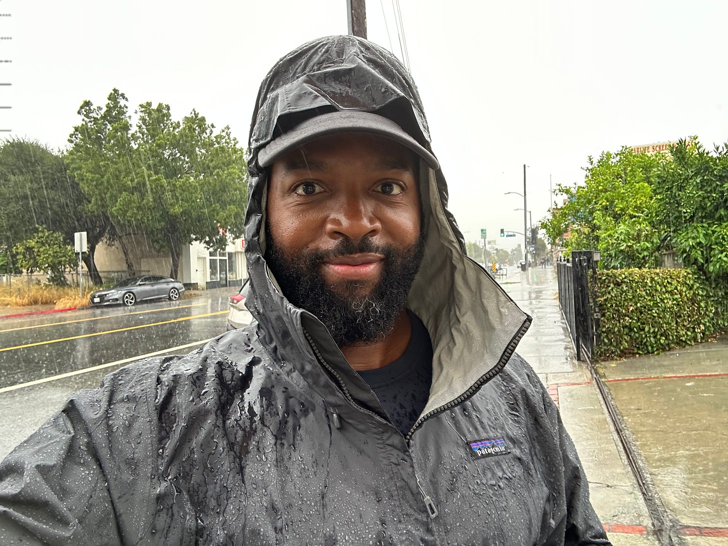 Baratunde in gray patagonia rain jacket during Tropical Storm Hilary downpour. looking at camera self satisfied. 