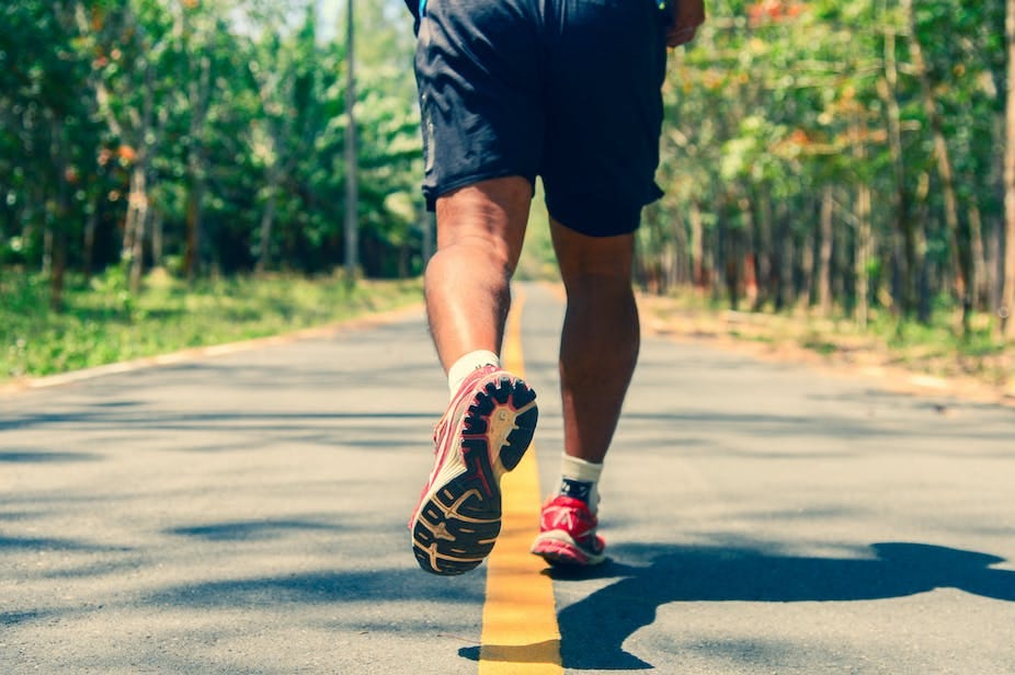 A photo of a man's legs and feet as he runs down an empty road.