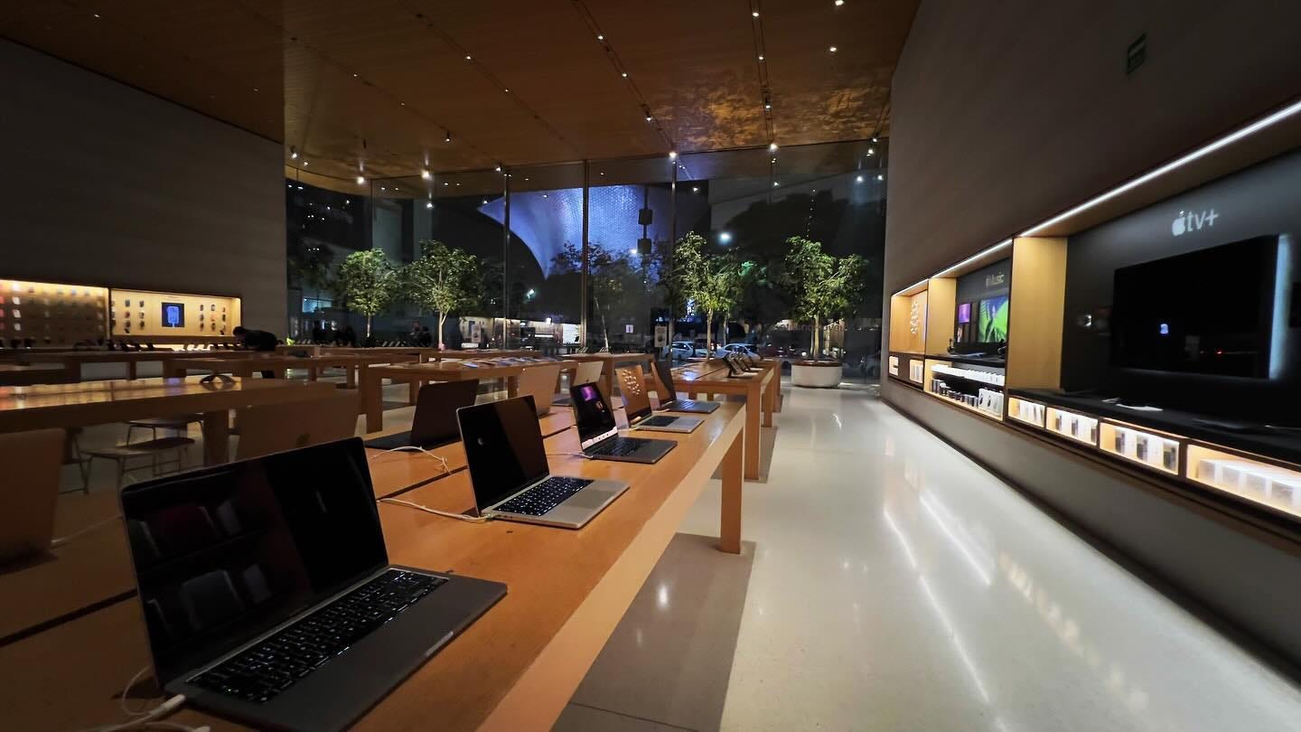 The interior of Apple Antara at night. The store lights have been dimmed and the demo Mac displays are powered off. The store has no people inside.