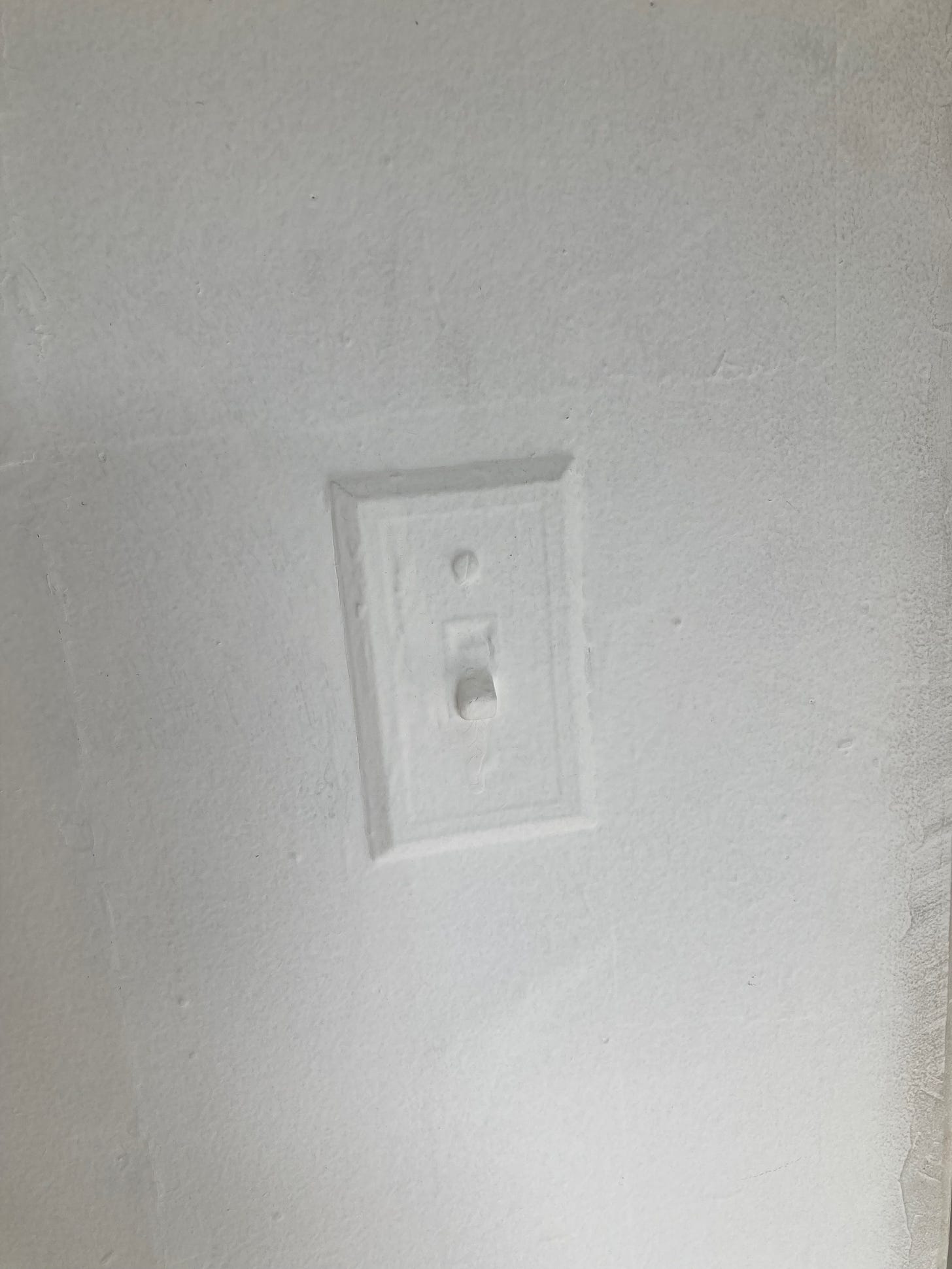 A lightswitch painted over - white walls, white paint covering all of it
