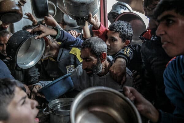 A crowd of men holding pots and pans as they try to collect food. 