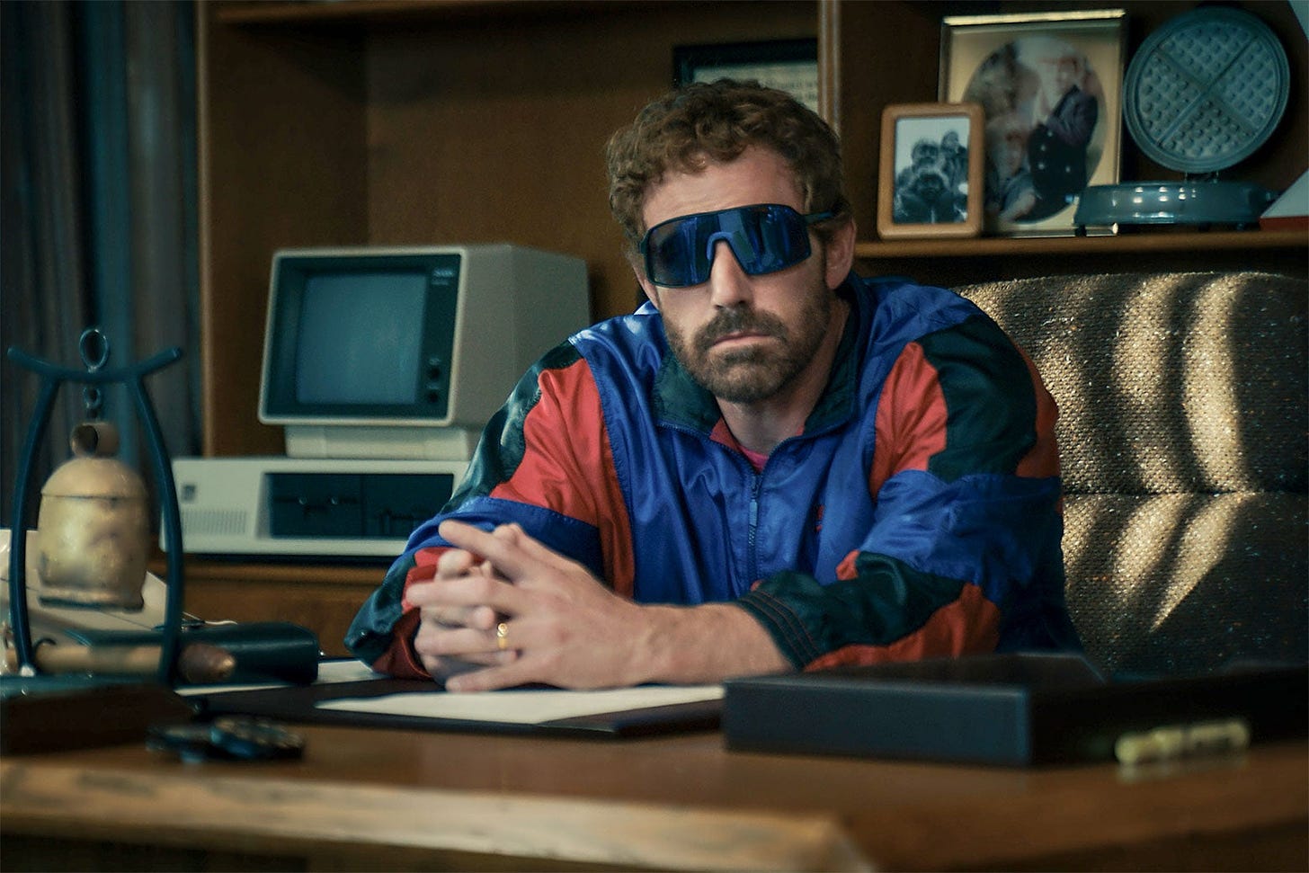 Ben Affleck as Phil Knight in Air. He has curly hair, is wearing big, wraparound sunglasses and a windbreaker.
