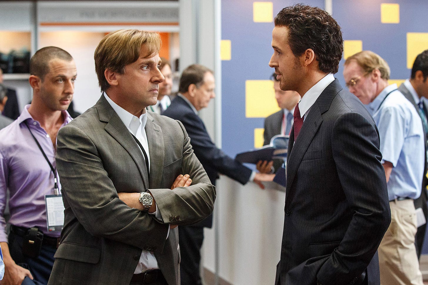 From The Big Short: Steve Carrel crosses his arms and looks perturbed at Ryan Gosling, who looks like he's got a golden ticket.