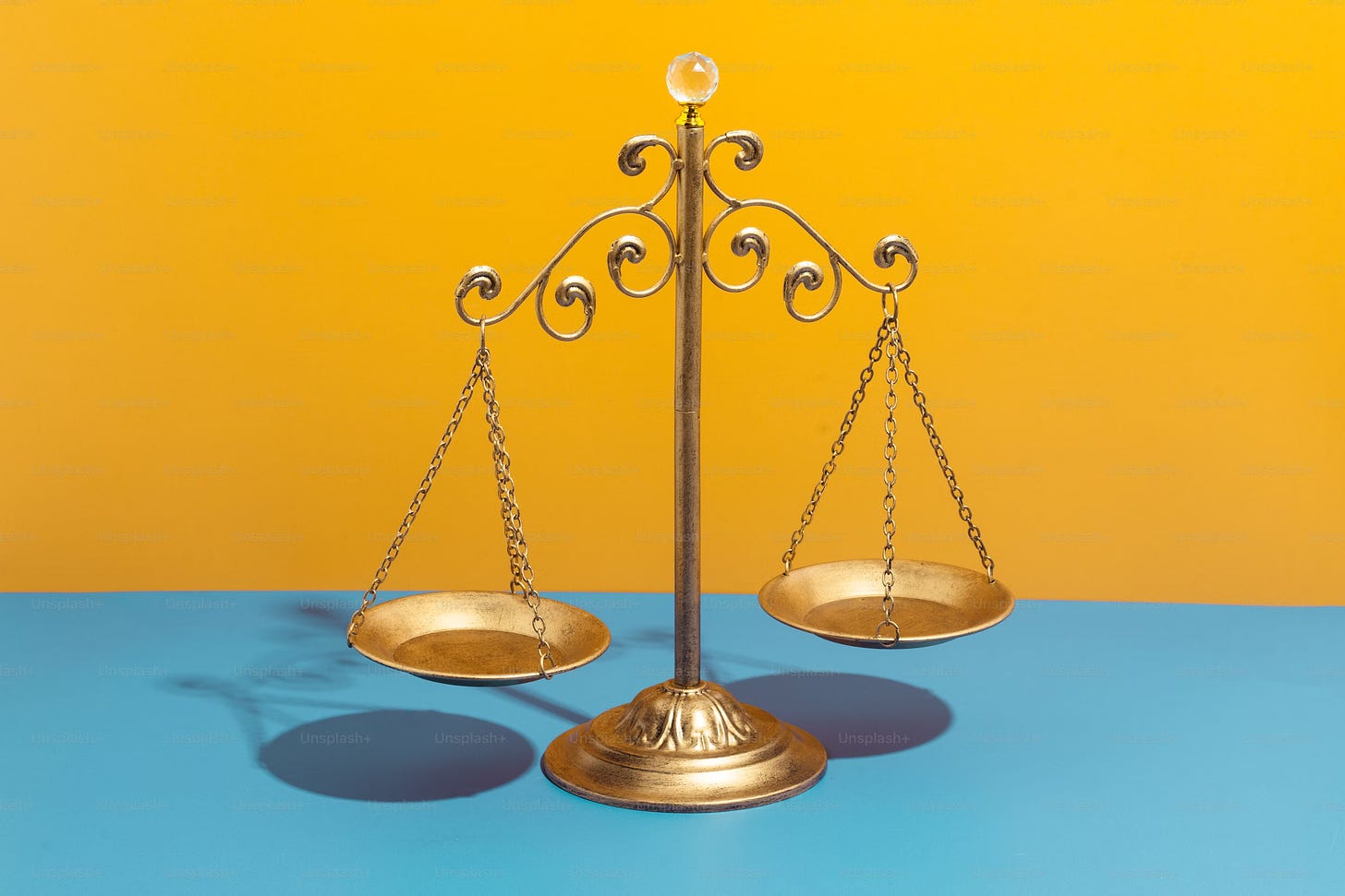 A gold variation on the scales of Justice sitting atop a blue surface on a yellow background.