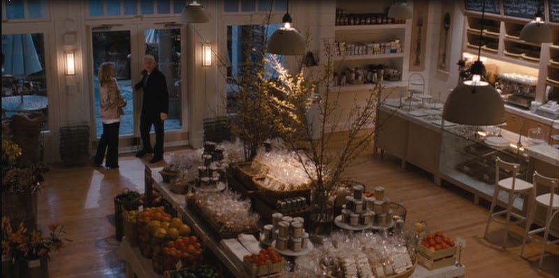 Movie still from It's Complicated. A fancy suburban kitchen is filled with delicious desserts, while a middle-aged couple chats by the door.