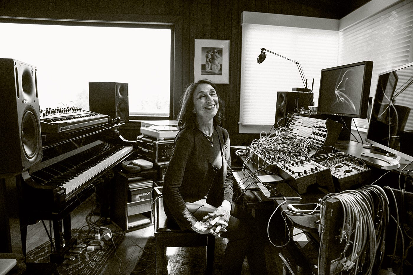 Suzanne Ciani poses in black and white at her music workstation, surrounded by a piano and a modular synthesizer.