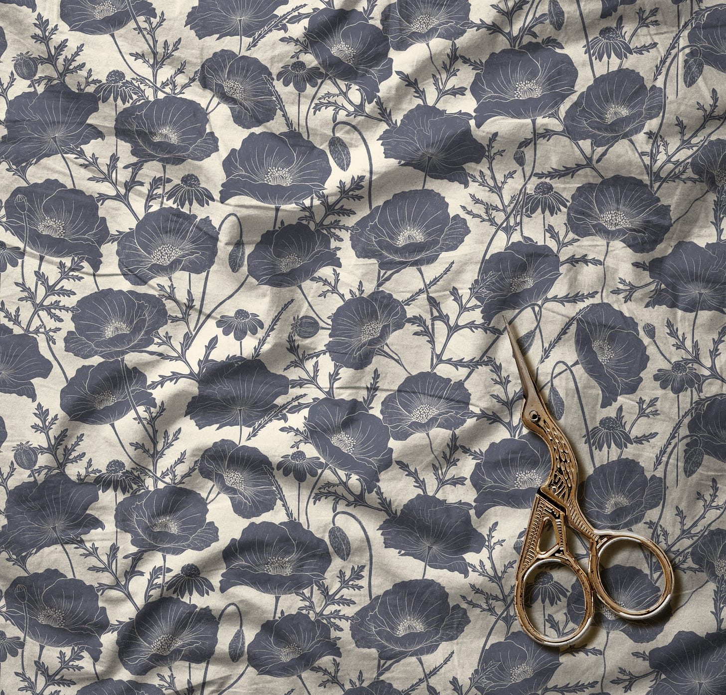 The new floral blue and white pattern mocked up as fabric. The fabric is spread out on a flat surface from edge to edge of the image, and on it rests a pair of scissors with a bird design on them. 