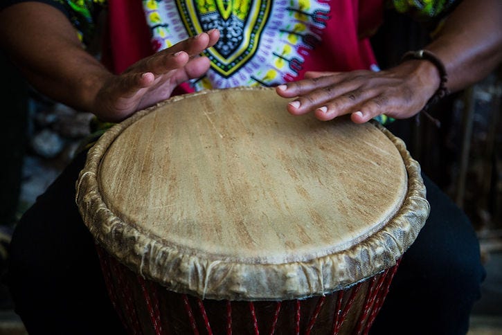 Image of a drum with a person beating drum with their hands.