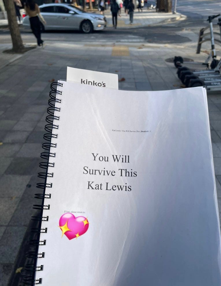 A photo of Kat’s printed novel manuscript for You Will Survive This. People on a Seoul city street are out of focus in the background.