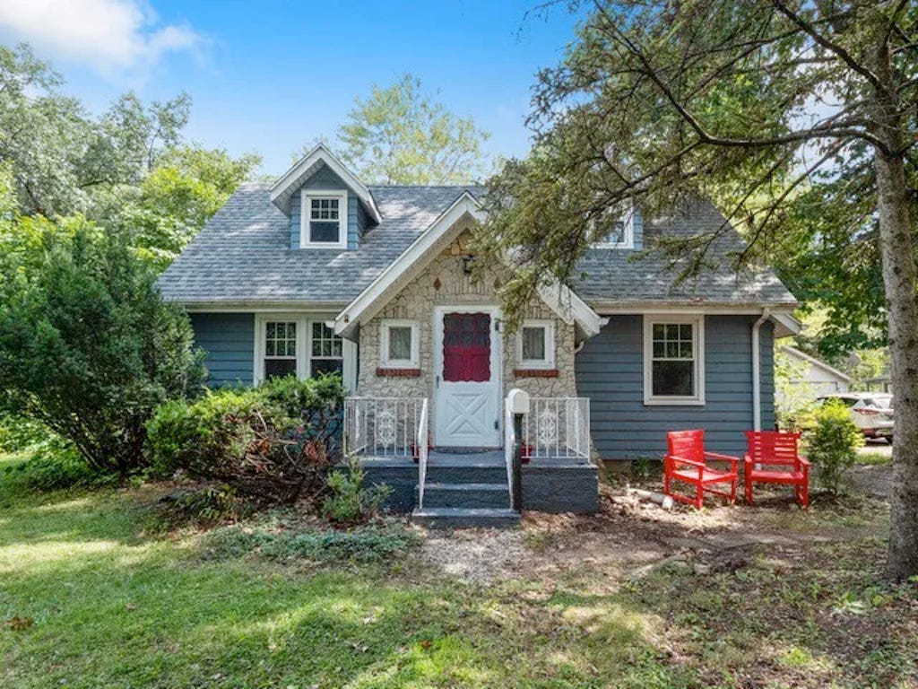 Adorable, tiny, Cape Cod style house with a stone facade surrounding the front door entrance.