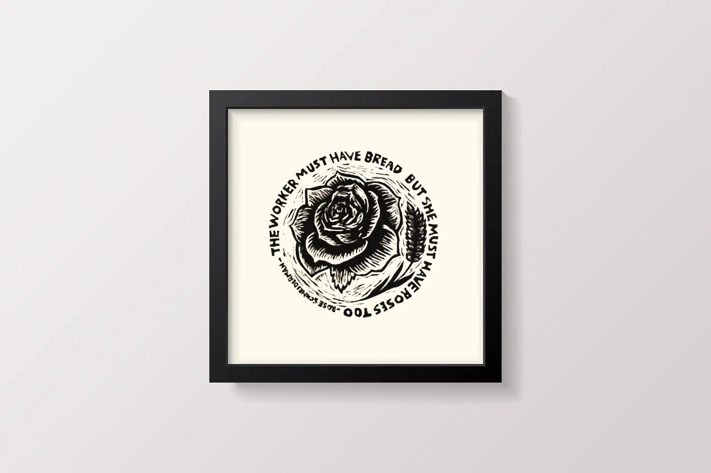 Linocut print in a frame with an image of a rose and a wheat grain that says "The worker must have bread but she must have roses too. -- Rose Schneiderman"