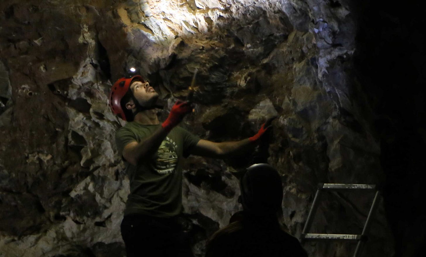 A man in caving helmet with light shining at cave ceiling