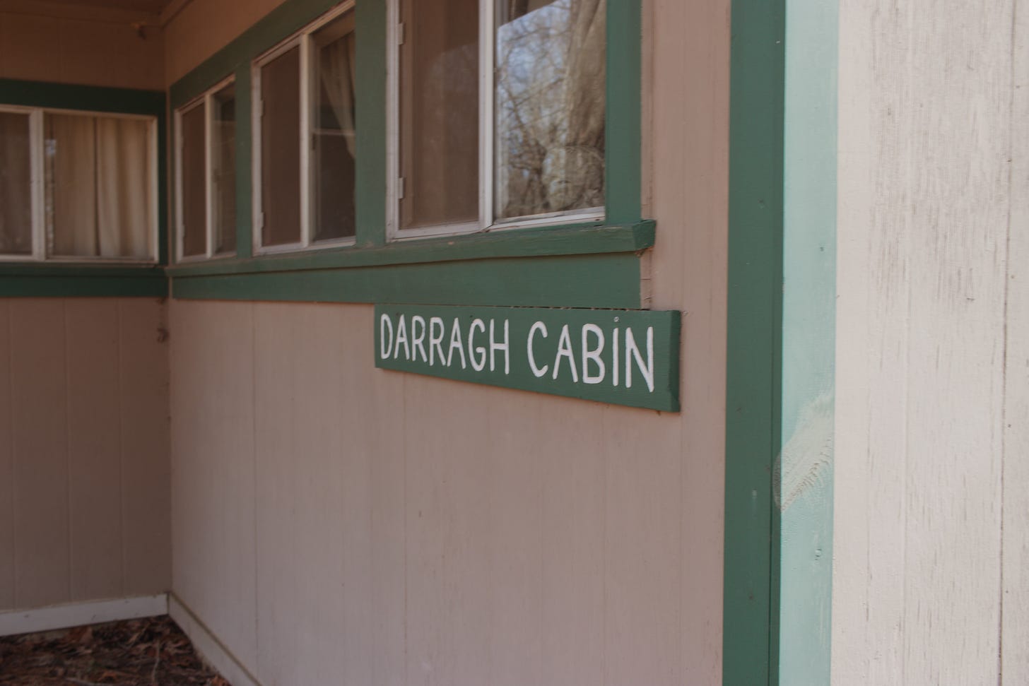 Grey brown camp cabin with green trim and a sign reading Darragh Cabin