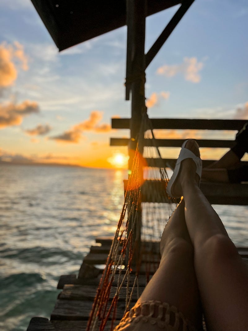 Legs up on a hammock against the sunset sky over the sea water