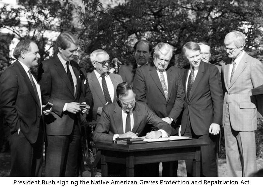 A group of men standing around a person signing a document

Description automatically generated