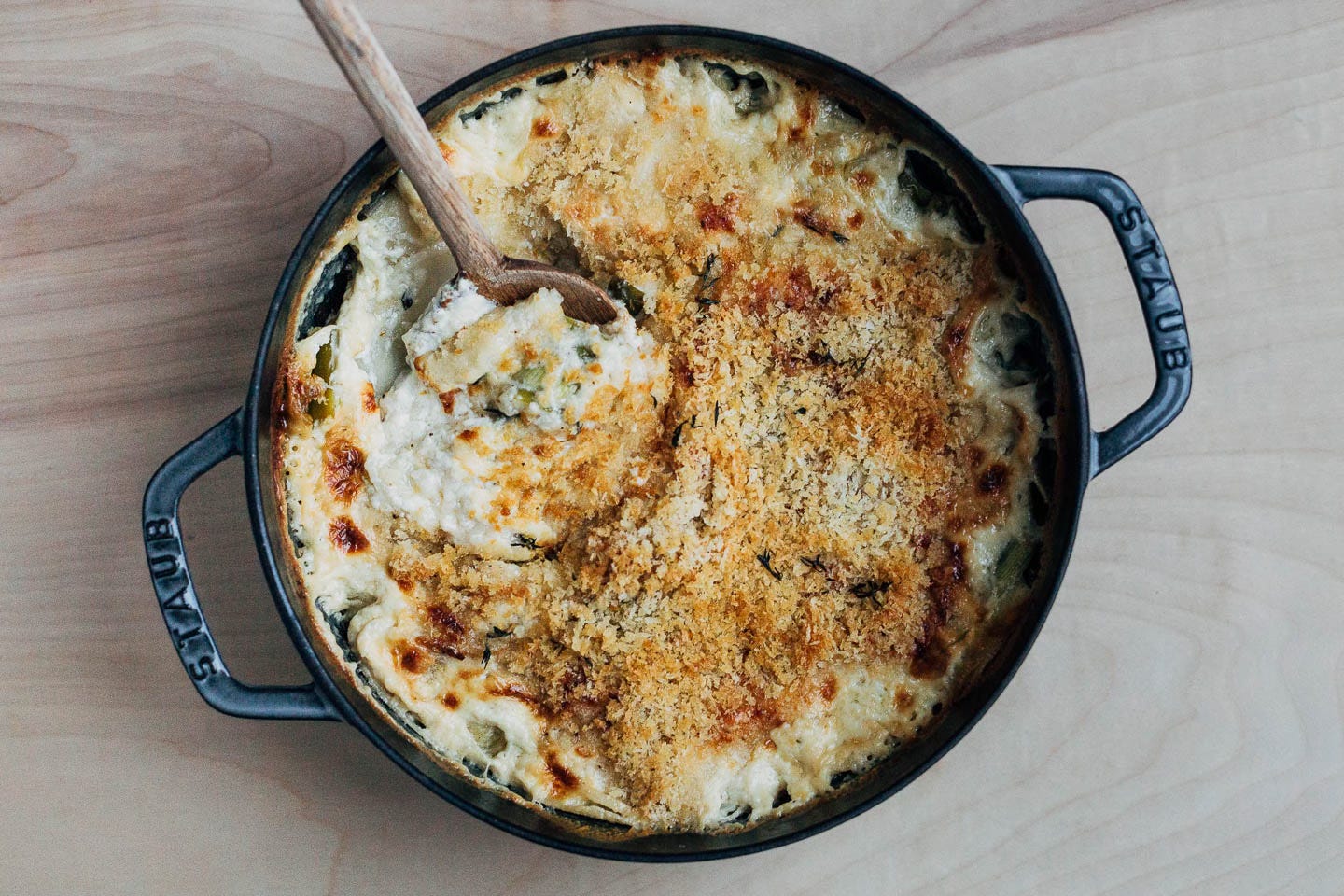 A spoon dipping into a baking dish filled with gratin. 