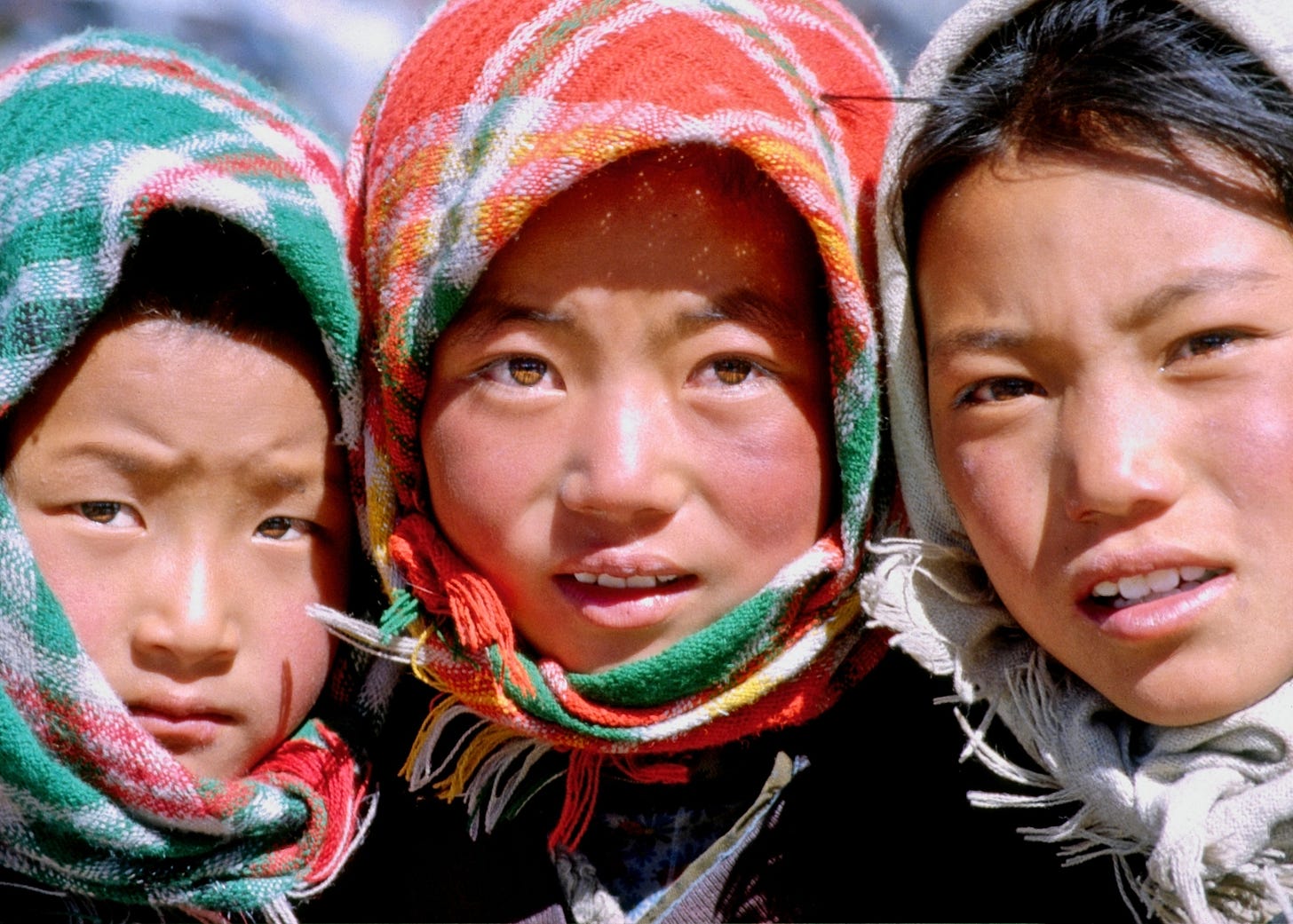 Close-up photograph: the faces of three children in headscarves