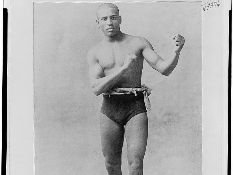 A black-and-white portrait photograph of African American boxer Joe Gans with his fists raised in a fighting pose.