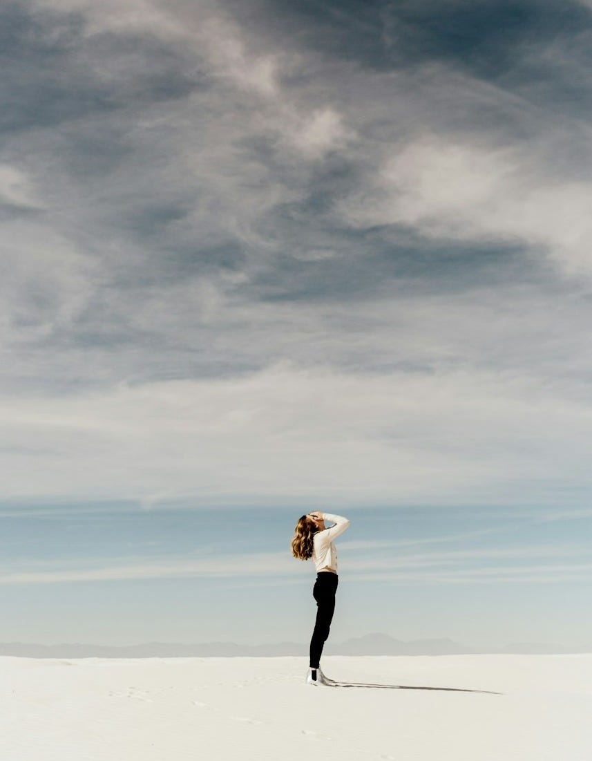 woman looking up to the sky while standing on white sand