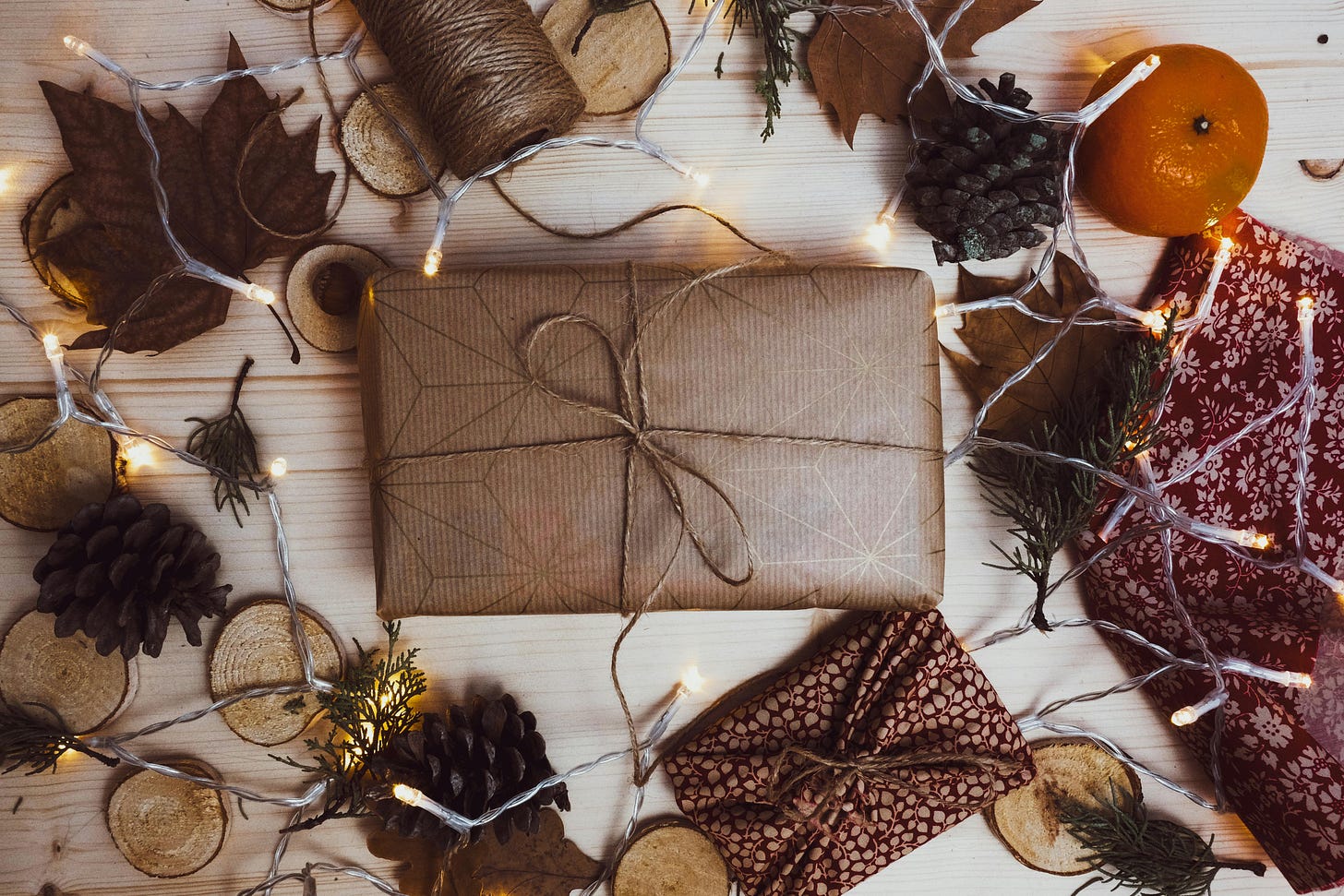 Flat lay of a gift wrapped in brown paper and autumnal accessories and Christmas lights placed around the edge