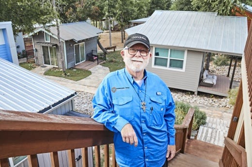 Photo of an older white man standing on an outdoor staircase with tiny homes in the background