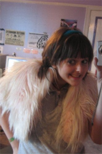 A young woman in a pink fluffy jacket posing in her bedroom with a digital camera