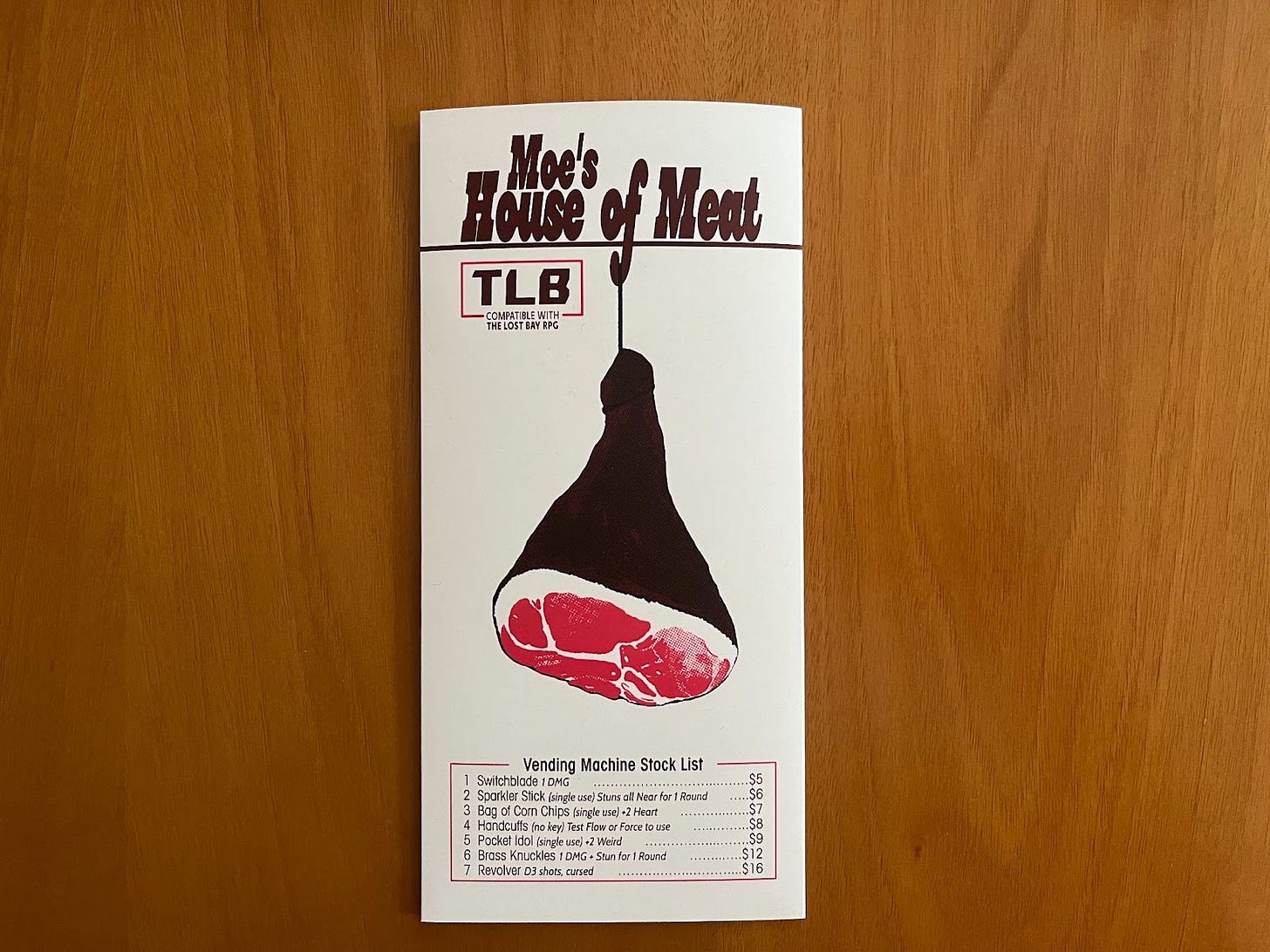 A physical copy of Moe’s House of Meat by Allen Hall. The cover is white with dark red text, and features a stylized illustration of a leg of meat.