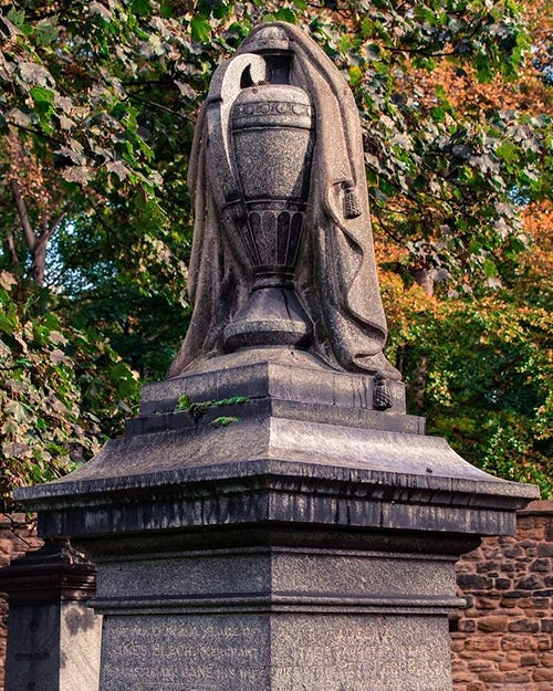 A stone urn with a piece of stone carved to look like cloth draped over it.