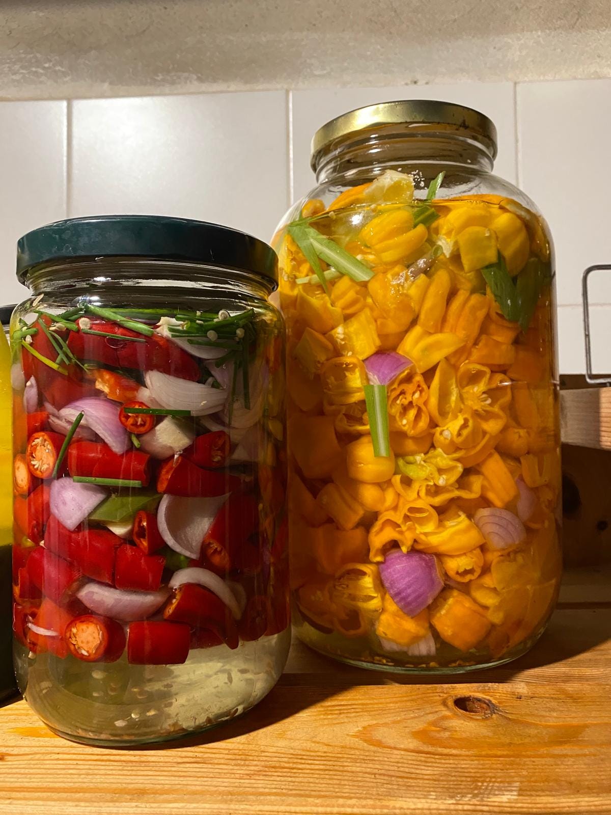 Two jars of hot peppers in brine - one is cayenne, bell pepper, onion, garlic, and chives, and the other is habanero, onion, orange, and lemongrass