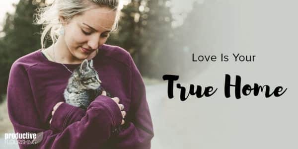 A blonde haired woman wears a sweater and holds a grey fluffy kitten in her arms. Text Overlay: Love Is Your True Home