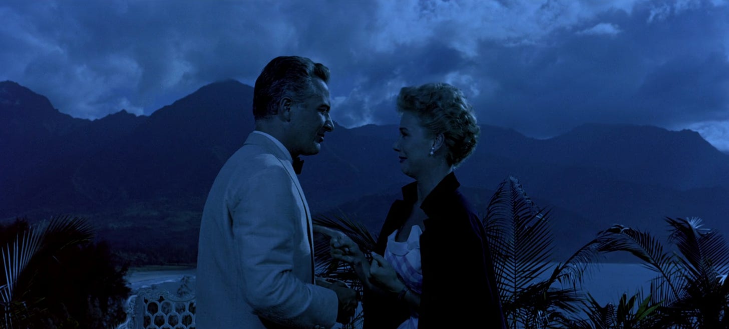 Rossano Brazzi as Emile de Becque and Mitzi Gaynor as Ensign Nellie Forbush in eveningwear against a romantic mountain backdrop with moonlit clouds in 1958 musical film South Pacific