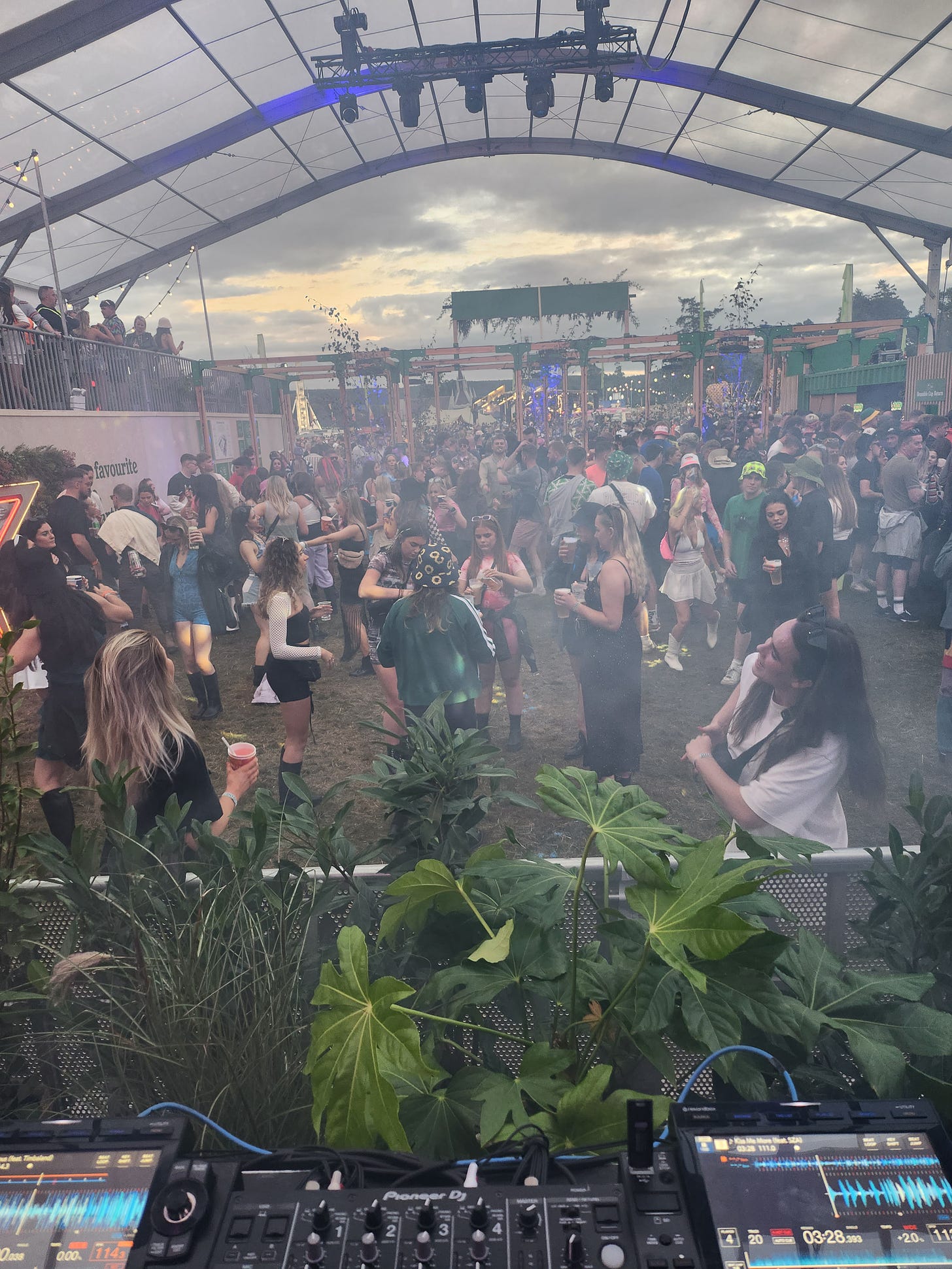 Taken from the stage and from behind a set of DJ decks, the photo shows a bunch of people (mostly gals) dancing in a Heineken branded tent. It's like a giant glasshouse, with a VIP area overlooking the dance floor. The sun sets on what feels like the first dry festival this summer. 