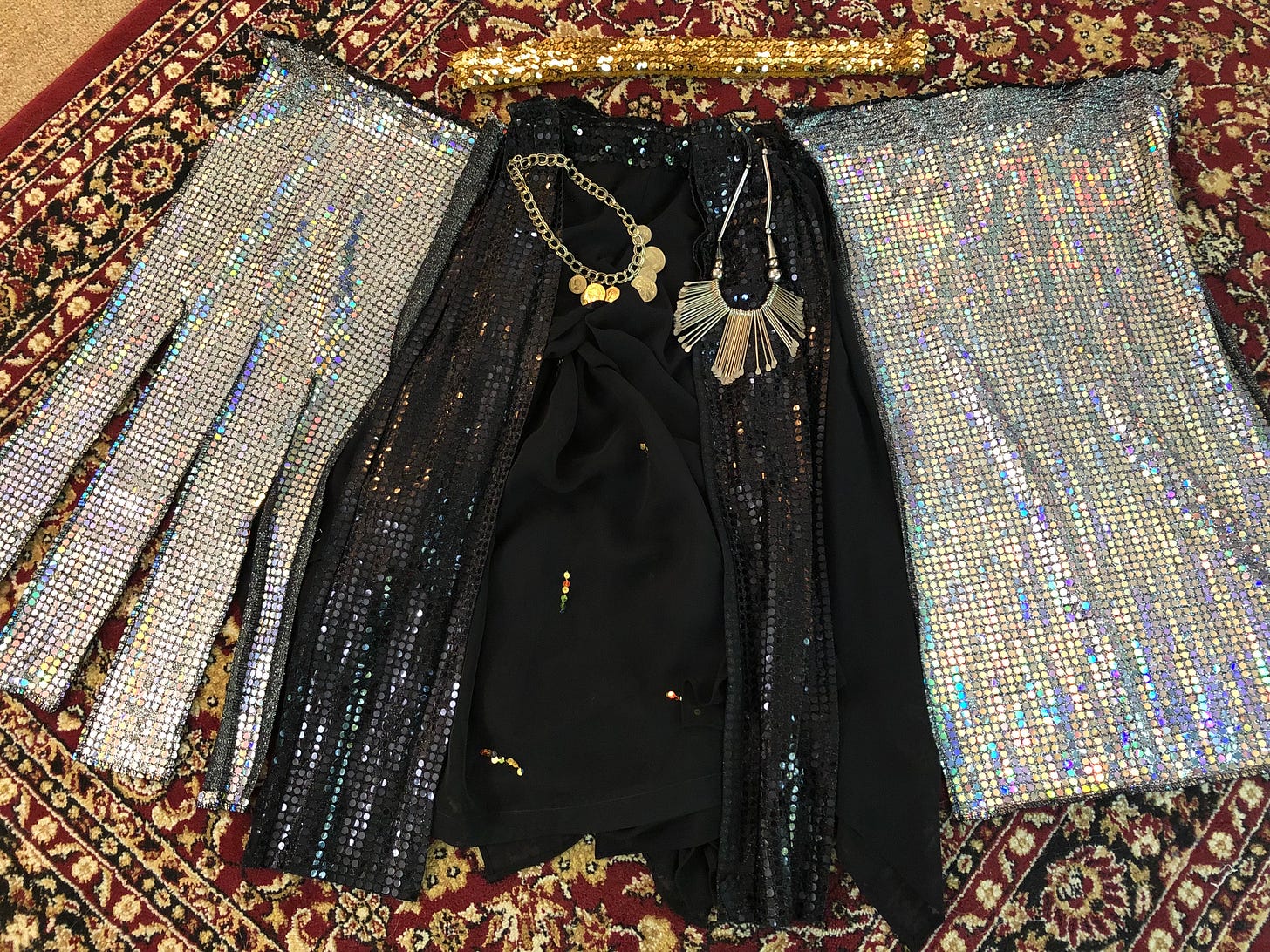 Holographic silver sequined panels flank skirts of sparkly black, with two gold necklaces and a gold sequin belt. They all lie spread across an ornate burgundy rug.