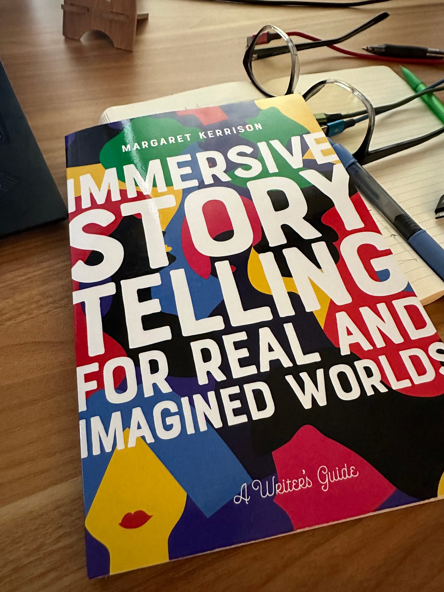 Copy of brightly colored book (Immersive Storytelling for Real and Imagined Worlds) sitting on a brown wood desk