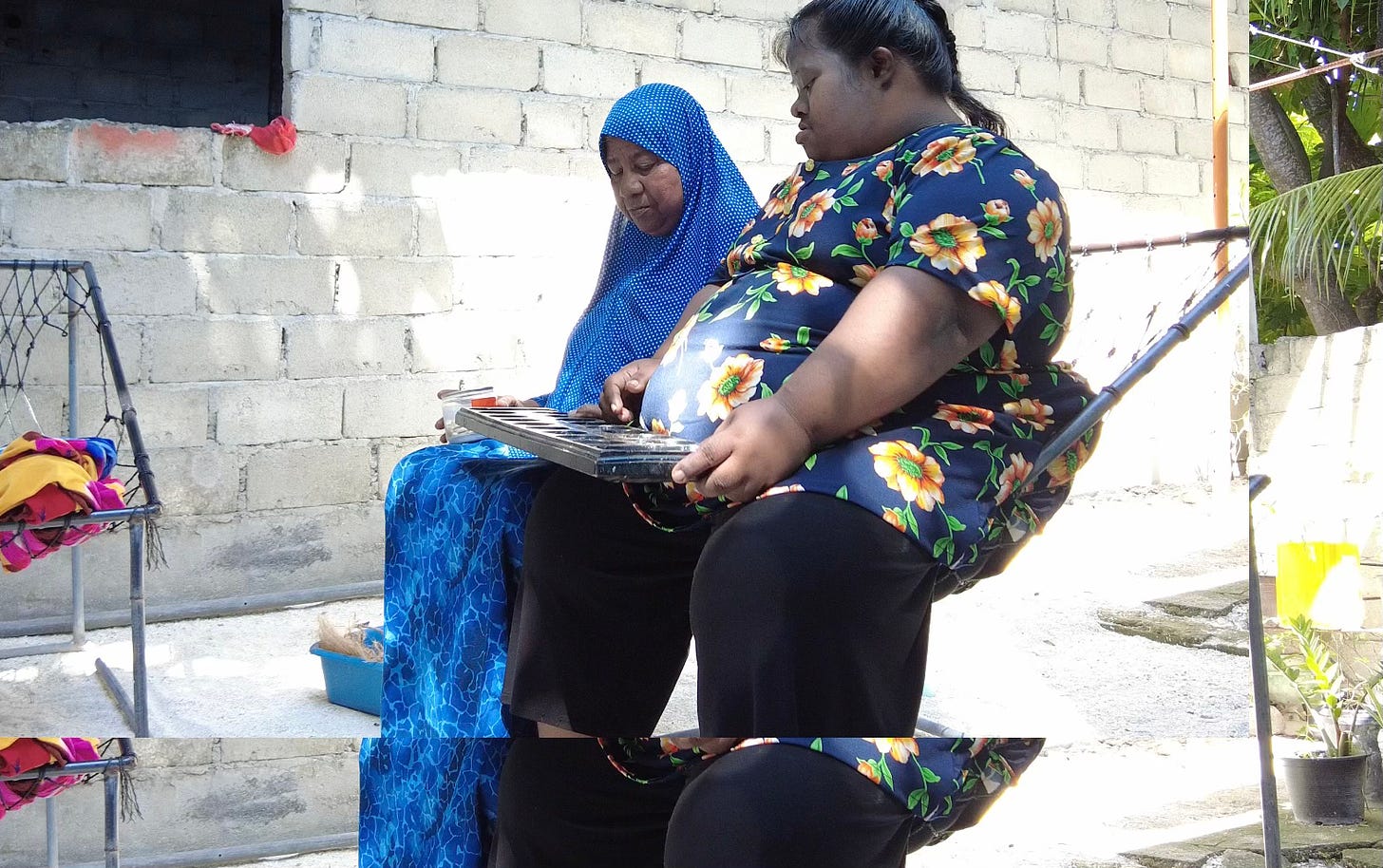 A woman wearing a blue hijab sits next to another woman, wearing a black, floral print shirt