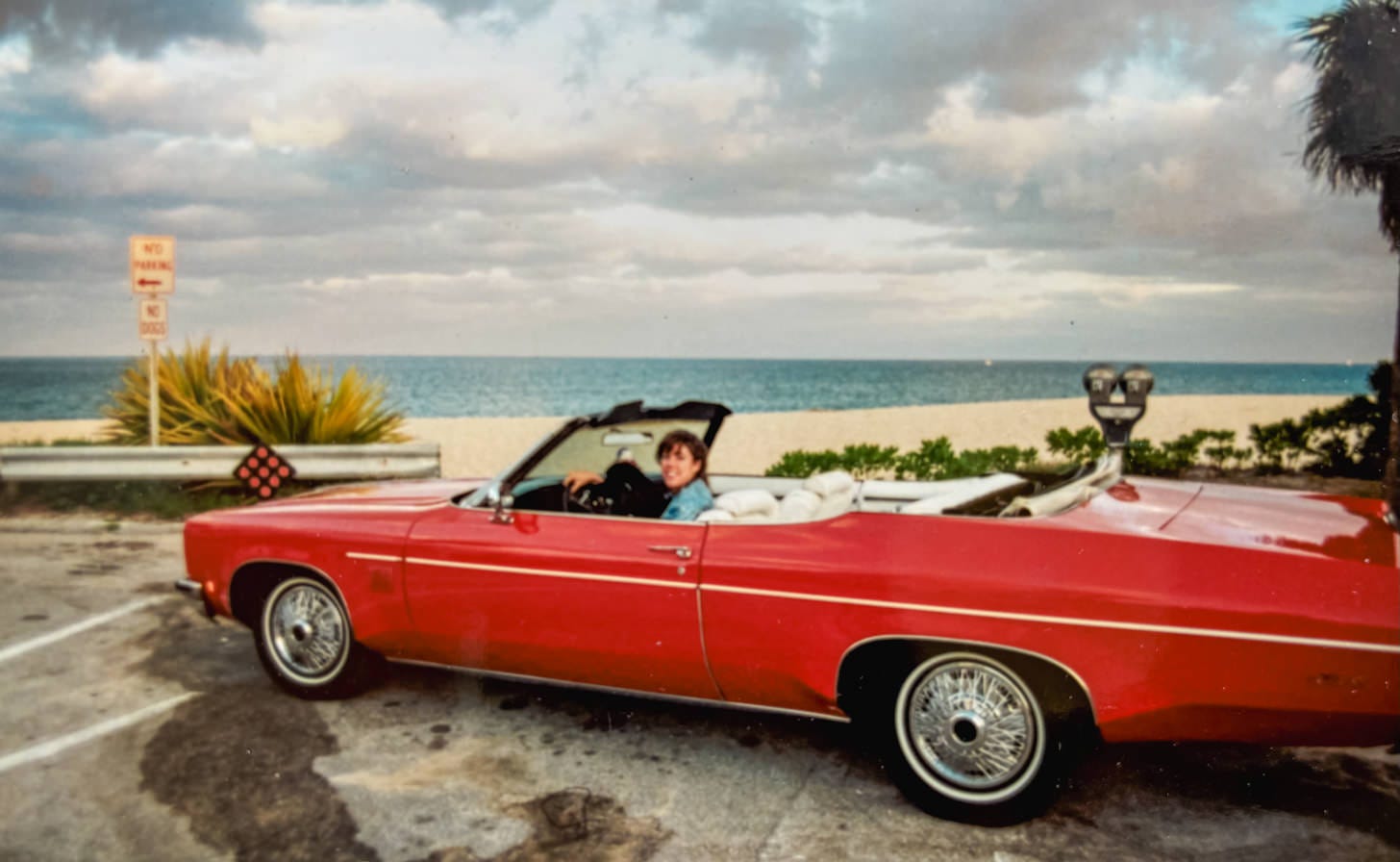 Woman in 1970's red convertible parked next to beach