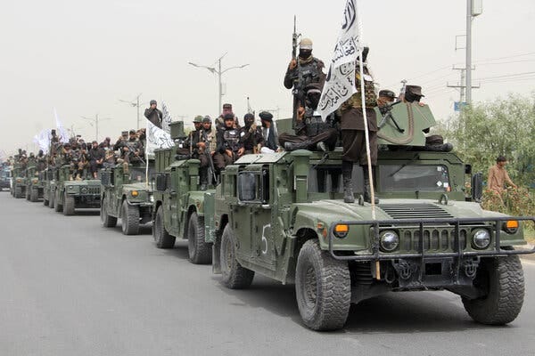 A line of military vehicles carrying armed Taliban fighters and the militants’ flags.