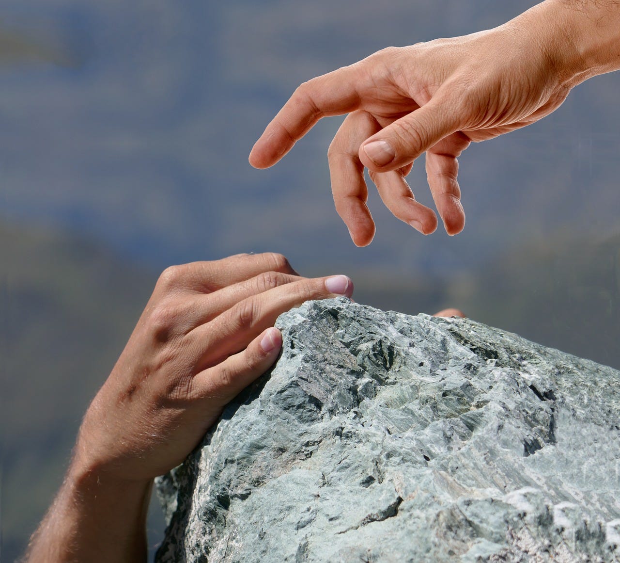Grey and blue rock climbing scene, with one hand holding onto the edge of a rock and the other hand reaching down to help