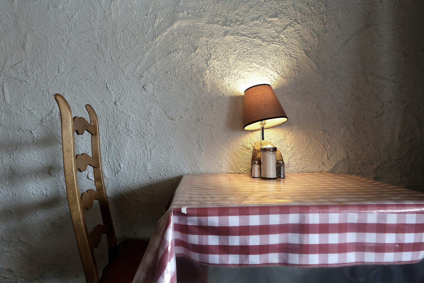 A classic Italian red-and-white checkered tablecloth at a corner table in a little restaurant. A small lamplight is on the inside of the table.