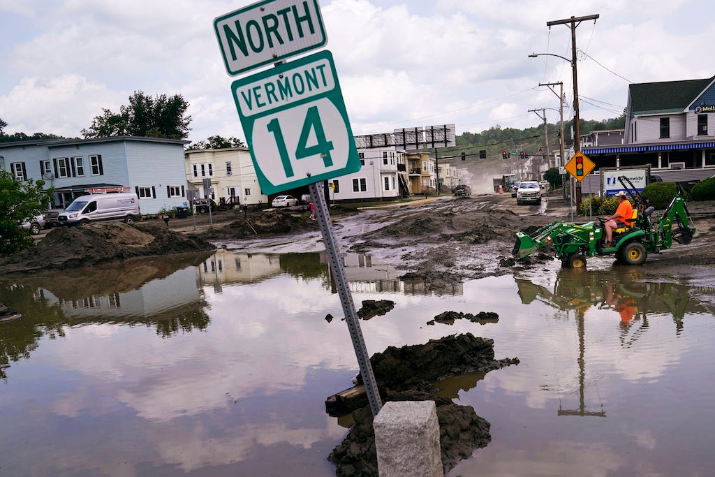 A small tractor clears water from a business as flood waters block a street, July 12, 2023, in Barre, Vermont.